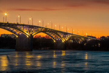 Obraz na płótnie Canvas Bridge at sunset, with yellow illumination, frozen river, ice.