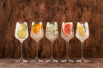 Gin and tonic cocktails set. Alcoholic drinks with lime, lemon, grapefruit, cucumber, soda and spicy herbs in wine glasses, wooden background. Summer cocktail party