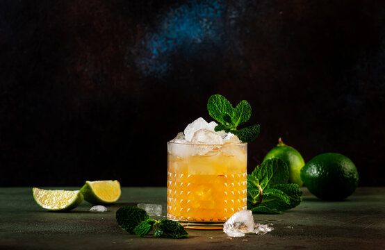 Mai Tai trendy alcoholic cocktail with rum, liqueur, syrup, lime juice, mint and crushed ice. Dark background, bar tools, copy space