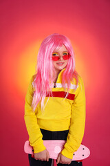 Cute indie girl with sunglasses and penny board on bright pink background