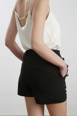 Female model wearing white camisole silk top and black tailored shorts. Classic summer fashion....