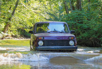 The Russian crossover wades through the river. The car drives along the river in the middle of the forest. © VeNN