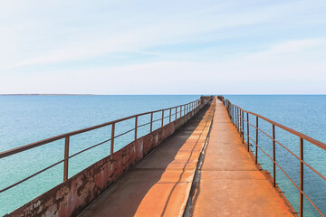 Obraz premium A long, rusty iron pier that goes far into the blue sea. A view from the pier into perspective. Seascape.