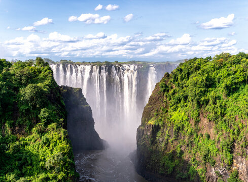Vast masses of water from the Zambezi River plunge over Victoria Falls, with the rainforests of Zimbabwe flanking the waterfall on both sides