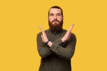 Serious bearded man is showing stop or x gesture made with arms.