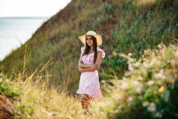Obraz premium the girl runs across the field. Happy girl. Long hair. White dress. A hat with a brim. Bouquet of daisies. A young girl in nature.