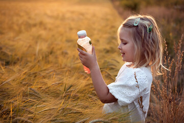 Little girl drinking refreshing fruit ice tea drink outdoors in summer. Country crop fields, golden hour sunset