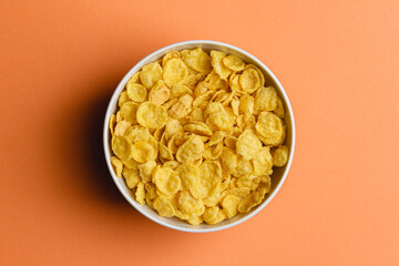Corn flakes in white bowl on orange background.