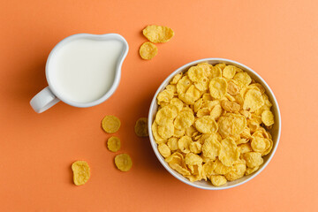 Corn flakes in white bowl and milk on orange background.