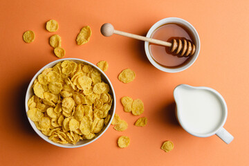 Corn flakes with milk and honey on orange background.