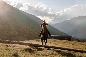 A rider on a horse jumps over a log gallops through a mountain valley