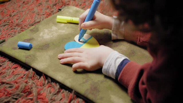 A child paints a heart in the colors of the flag of Ukraine, side view