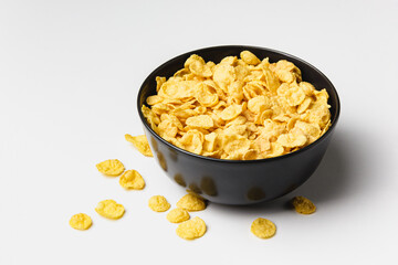 Corn flakes in dark bowl on white background.