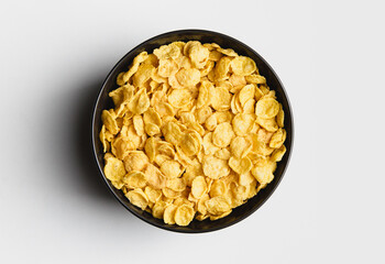 Corn flakes in dark bowl on white background.