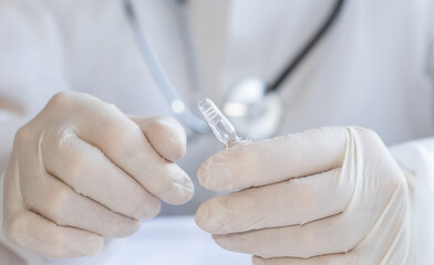 female hands are opening a glass ampoule with medicine. doctor or nurse is in white disposable robe...
