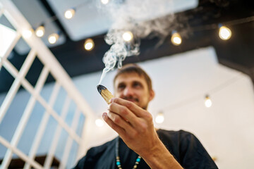 A man holds a piece of wood Palo Santo. Lots of fragrant smoke