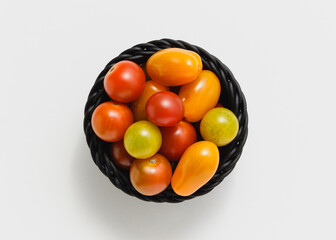 Cherry tomatoes in black basket on white background.
