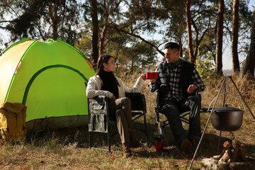Couple sitting in camping chairs and clinking mugs outdoors