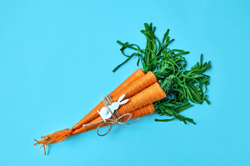 Bunny rabbit ears and craft wool thread carrots on light blue background. Minimalist decor for Easter. Handmade craft project. Concept of holiday and shopping for Easter.
