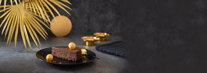Chocolate cheesecake banner. Piece of chocolate cake decorated with golden truffle on a black plate. Copy space. Confectionery, bakery web line. No bake chocolate mousse dessert recipe