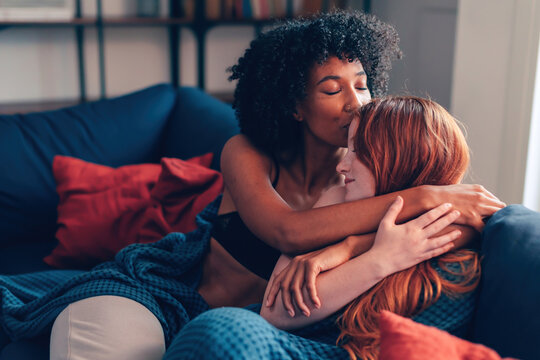 girls bonding and cuddling on the sofa - romantic sapphic love between women of different ethnicities on couch