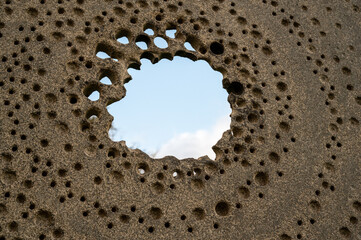 An old stone wall with holes in a circle through which you can see the sky.