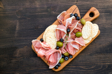 Italian ham prosciutto or spanish jamon with olives and crackers on a wooden plate. Food for an...