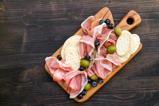 Italian ham prosciutto or spanish jamon with olives and crackers on a wooden plate. Food for an aperitif and dinner lunch in the restaurant. 