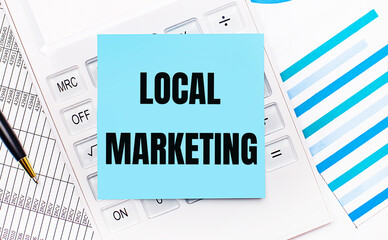 On the desktop is a white calculator with a blue sticker with the text LOCAL MARKETING, a pen and blue reports. Business concept
