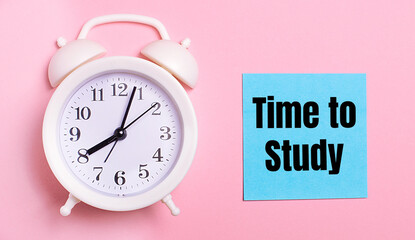 On a light pink background, a white alarm clock and a blue sheet of paper with the text TIME TO STUDY