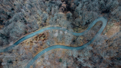 Aerial high angle view of narrow winding curvy mountain road among the trees in winter forest. Bird's eye view landscape.
