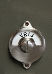 a metal revolving sign on a door with the dutch inscription Vrij, which means not occupied