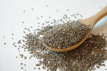 Chia seeds in a wooden spoon on a white background.