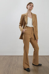 Female model wearing beige tailored suit and white silk top. Studio shot.