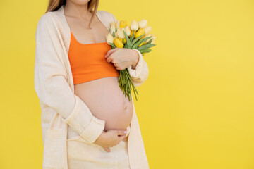 Portrait of unrecognizable pregnant woman wear orange top, beige cardigan, trousers, holding bunch...