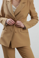 Female model wearing beige tailored suit and white silk top. Studio shot.