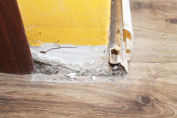 A fragment of a broken white plinth on a brown laminate and a yellow wall, close-up, side view. Under the plinth debris and dust. Dirty. Repair. Needs to be fixed. Man's work. House.
