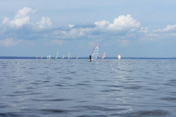 A group of people are windsurfing on calm water against a beautiful cloudy sky