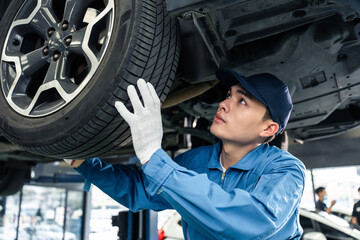 Asian automotive mechanic repairman look under car condition in garage