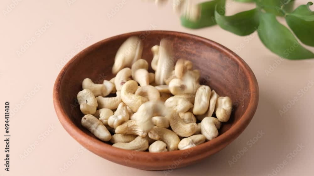 Wall mural cashew nuts in a bowl on beige background. slow motion cashews falling