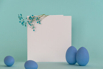 Easter mockup with decorative blue eggs and twigs of blue flowers placed near white square blank card