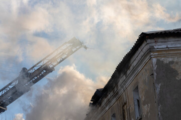 Firefighter works on boom of fire engine. Fireman on sky background. Burning old building in the historic center..Rescuers on a retractable ladder in the smoke.