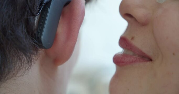 Woman speaks into the ear of a man who has a cochlear implant. Checks rumors reports personal information