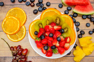 Fresh fruits concept, Tropical fruits and assorted berry salad in bowl on wooden background