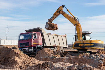 A powerful crawler excavator loads the earth into a dump truck against the blue sky. Development...