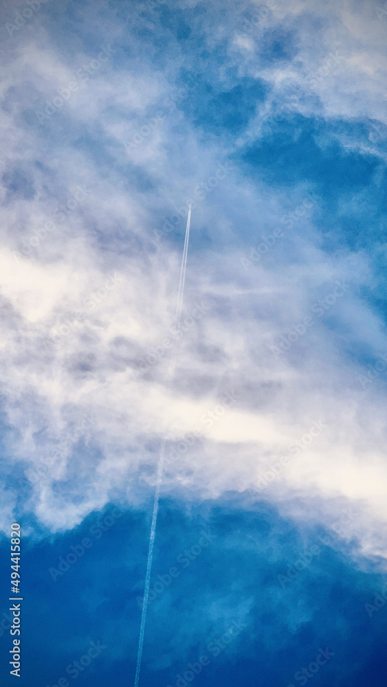 Sticker beautiful vertical shot of an airplane crossing the blue-white cloudy sky