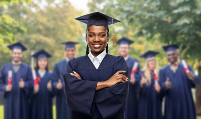 education, graduation and people concept - happy graduate student woman in mortarboard and gown over group of bachelors at park on background