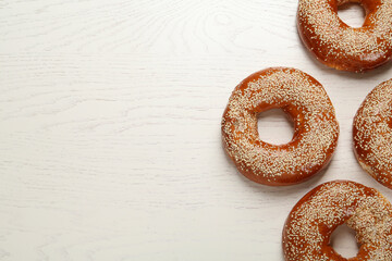 Delicious fresh bagels with sesame seeds on white wooden table, flat lay. Space for text