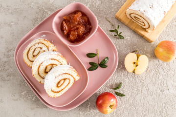 fresh apples and pieces of homemade sponge cake roll in powdered sugar on a pink ceramic tray. top view.
