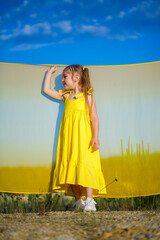 Obraz premium Ukrainian girl 7 years old, she is a patriot of Ukraine, dressed in a yellow dress against a blue sky. Blue sky. Sunny day. Free Ukrainian child. Child symbol of Ukraine